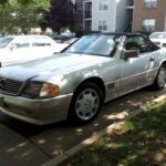 Front quarter view of a silver 1995 Mercedes Benz SL500 parked on a residential street, showcasing its classic roadster styling.