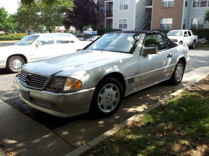 Front quarter view of a silver 1995 Mercedes-Benz SL500 parked on a paved area, showcasing its clean lines and five-spoke wheels.