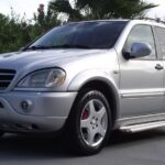 Front view of a silver 2001 Mercedes ML55 AMG parked on a paved surface, showcasing its aggressive AMG styling and five-spoke wheels.