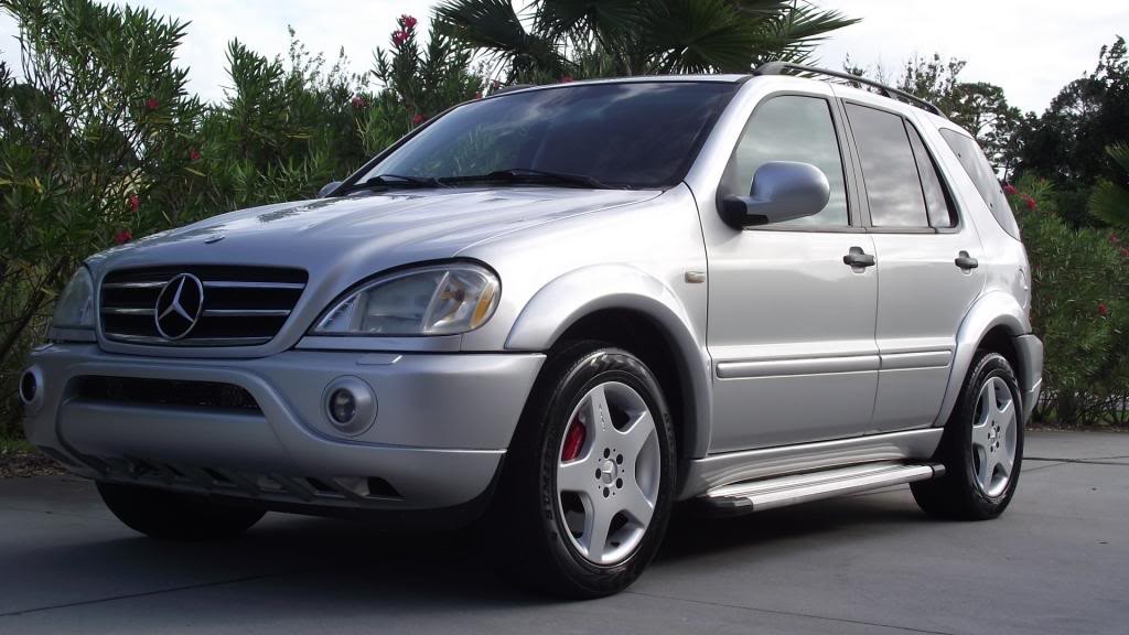 Front view of a silver 2001 Mercedes ML55 AMG parked on a paved surface, showcasing its aggressive AMG styling and five-spoke wheels.