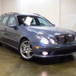 Front side view of a silver Mercedes-Benz E55 AMG wagon parked outdoors, showcasing its sporty yet understated design.