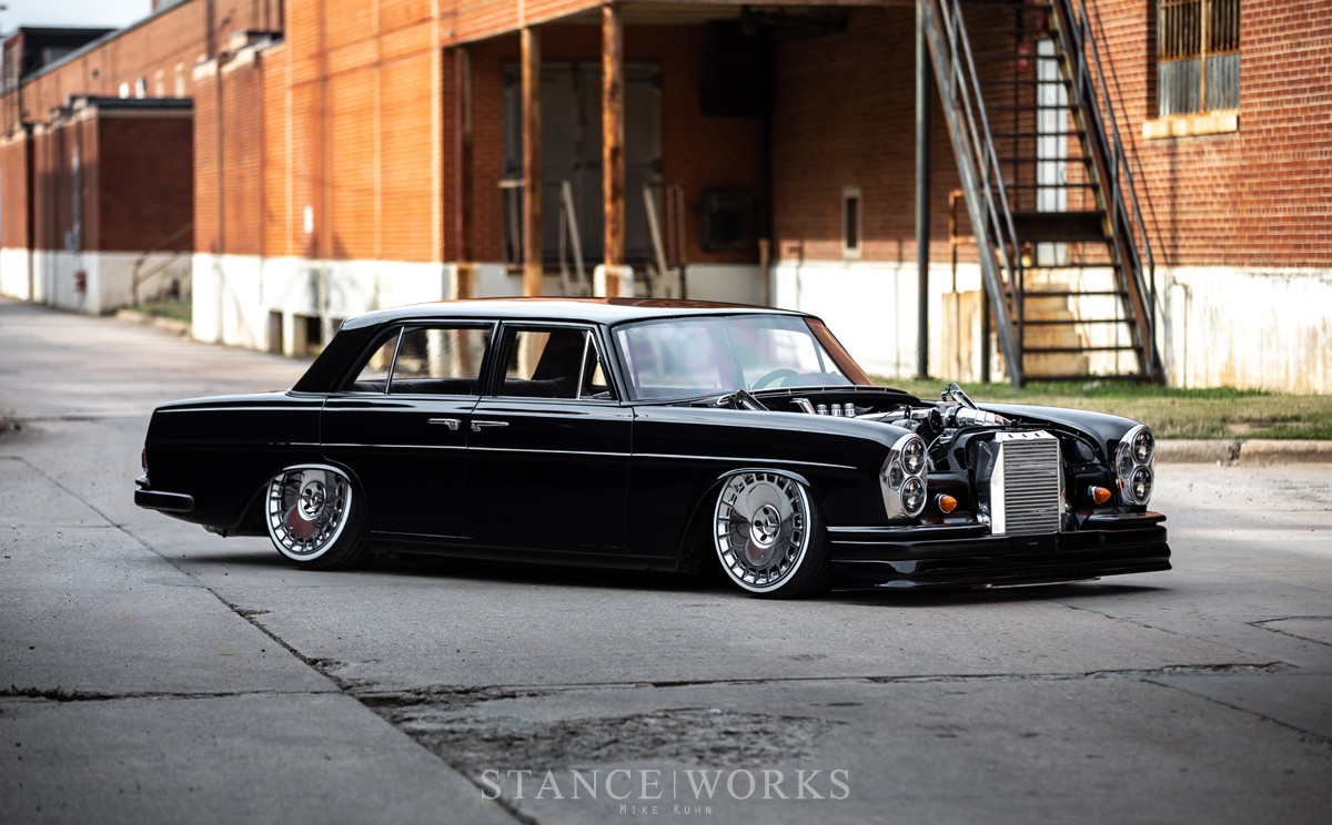 Front three-quarter view of a lowered, modified 1969 Mercedes 280S showcasing its custom wheels and aggressive stance.