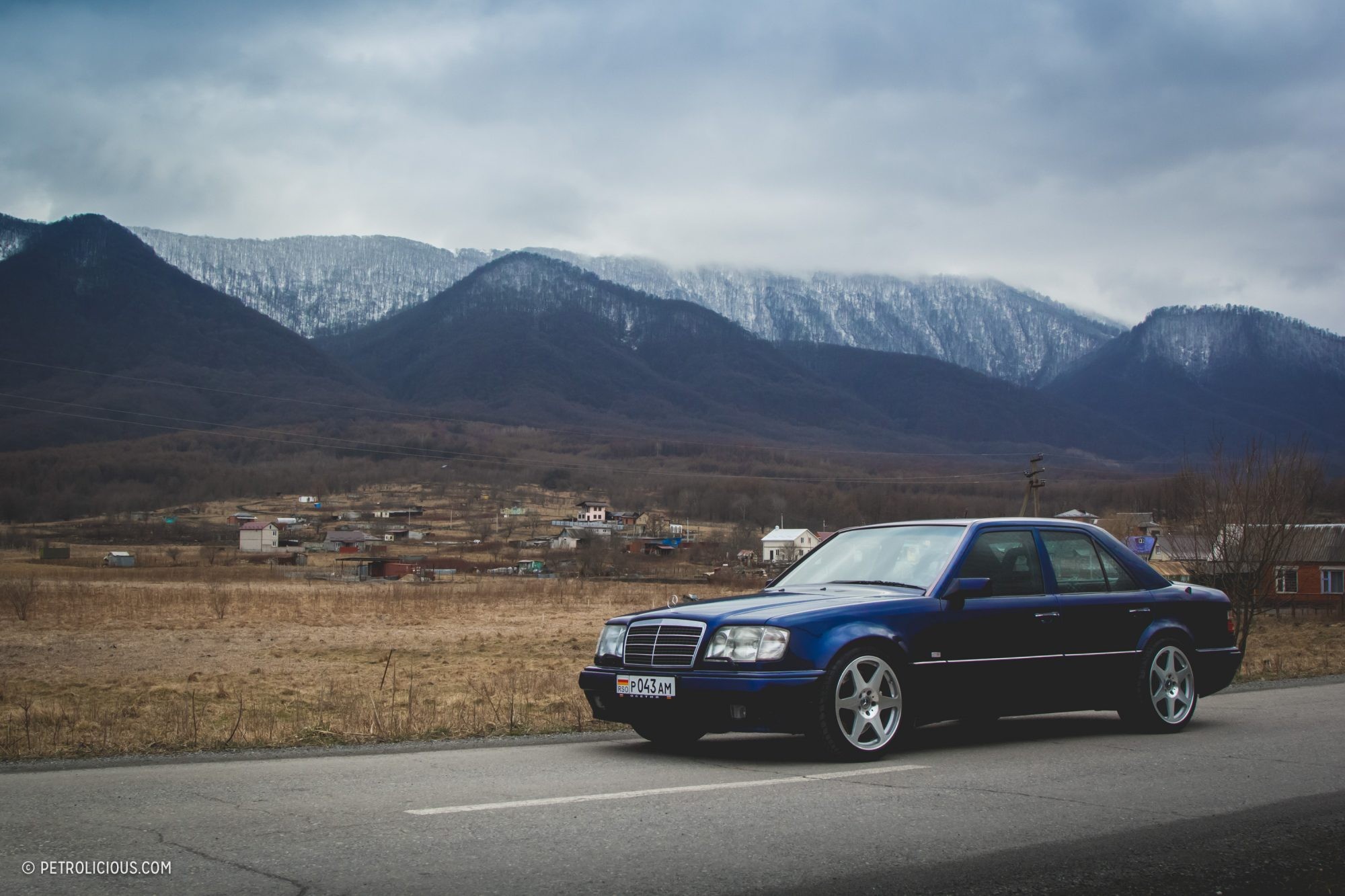 Front three quarter view of a dark blue Mercedes-Benz E60 AMG parked outdoors, showcasing its classic sedan silhouette.