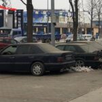 Collection of black Mercedes-Benz cars parked on a snowy pavement in front of car repair shops, suggesting an abandoned Mercedes dealership.