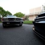 Front quarter view of a grey Mercedes 450 SLC 5.0 parked with the Menil Museum in the background, showcasing its long coupe silhouette