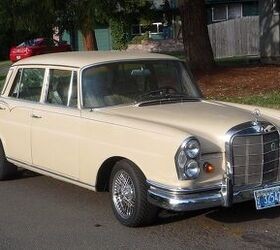 Front three quarter view of a black 1965 Mercedes 220S W111 with wire wheels parked on a street.