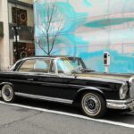 Front quarter view of a black Mercedes-Benz 220 Classic Coupe showcasing its Euro headlights and elegant design