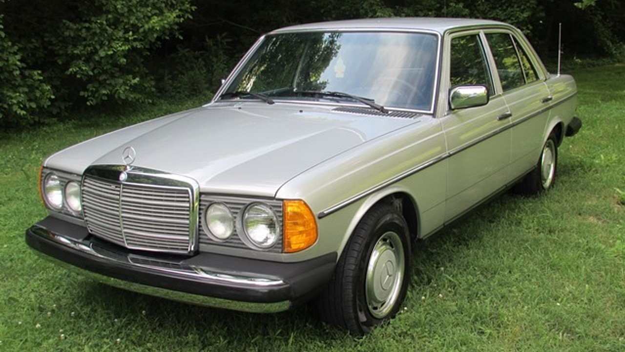 Front side view of a faded red 1980 Mercedes-Benz 300D with fog lights on a paved lot, showcasing its weathered paint condition.