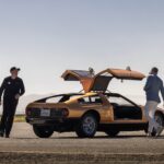 Mercedes-Benz C111 concept car in orange, parked on an airport tarmac with private jets in the background, showcasing its wedge shape and classic design.