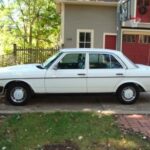 Front quarter view of a white 1983 Mercedes-Benz 240D parked on a paved surface, showcasing its classic sedan profile and iconic Mercedes grille.