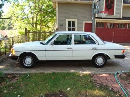 Front quarter view of a white 1983 Mercedes-Benz 240D parked on a paved surface, showcasing its classic sedan profile and iconic Mercedes grille.