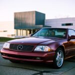 Front three quarter view of a Firemist Red 2002 Mercedes Benz SL500 parked in an urban setting, highlighting its sleek design and convertible top.