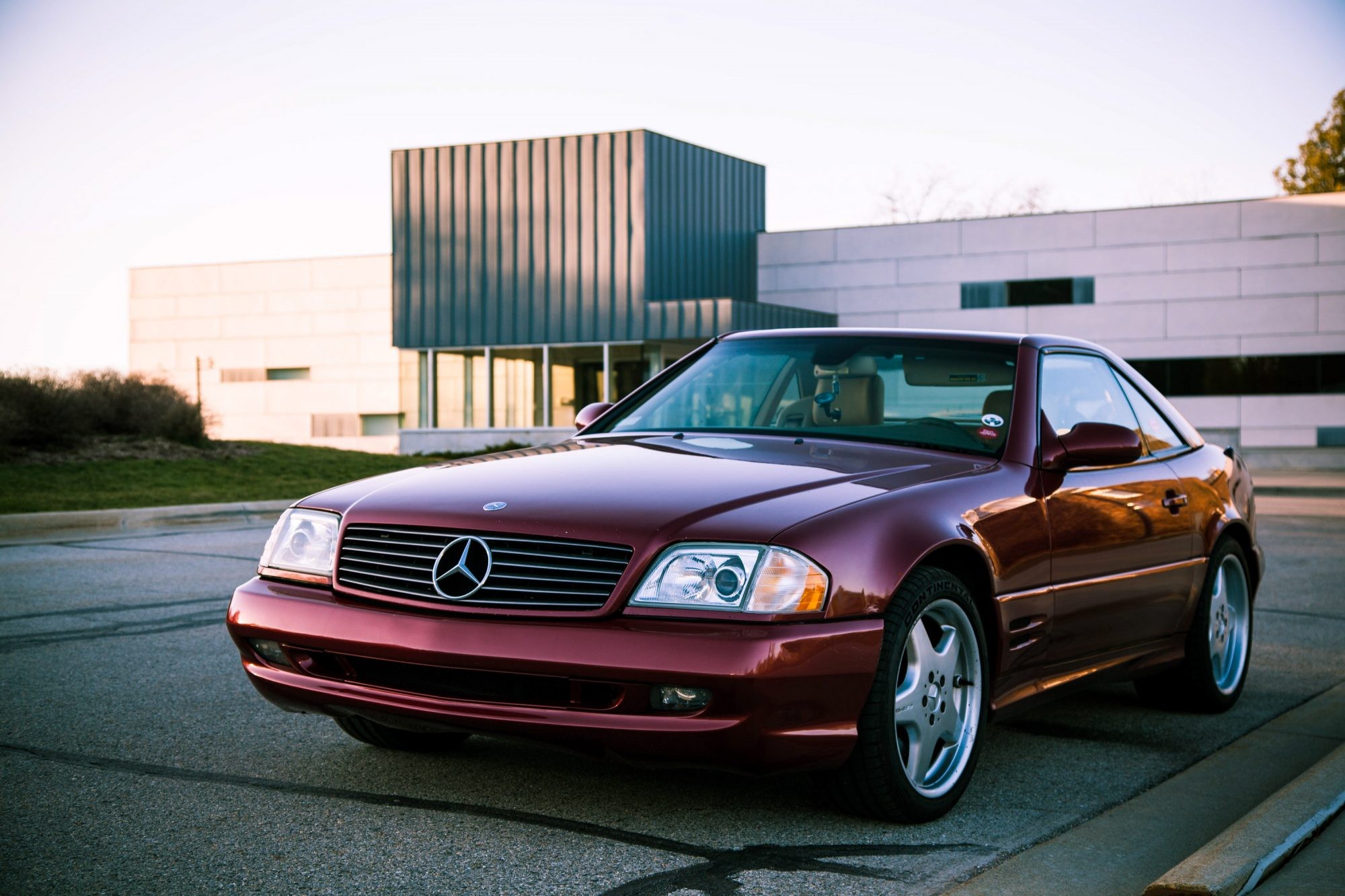 Front three quarter view of a Firemist Red 2002 Mercedes Benz SL500 parked in an urban setting, highlighting its sleek design and convertible top.